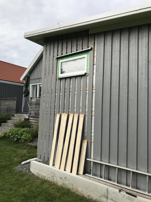 Husfasad under renovering med påbörjad panel, läkt och fönsterplåtar synliga.