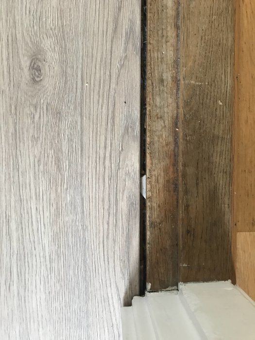 Större glapp mellan trägolvet och en tröskel i ett hus, behov av en kil-list för täckning.