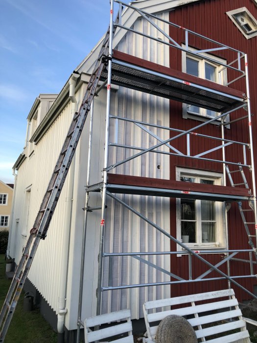 Ställning och stege framför röd träfasad med nygrundmålad yta under renovering.