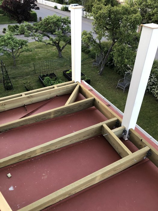 Uppifrån bild av ett pågående bygge av balkongbjälklag i trä på en röd terrass, med vy över en trädgård.