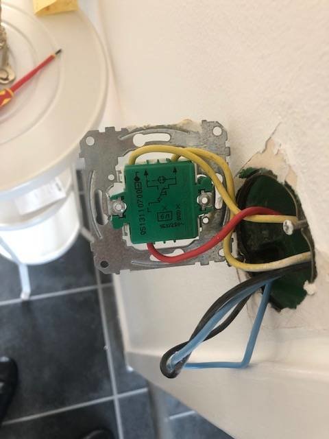 Omonterad vägguttag med exponerade elledningar och anslutningsschema, monteringsarbete pågår.