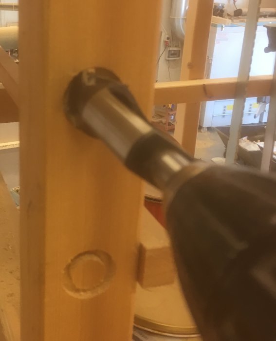 En handhållen borr med pluggborrborren närmar sig ett trästycke där ett hål precis börjat borras.