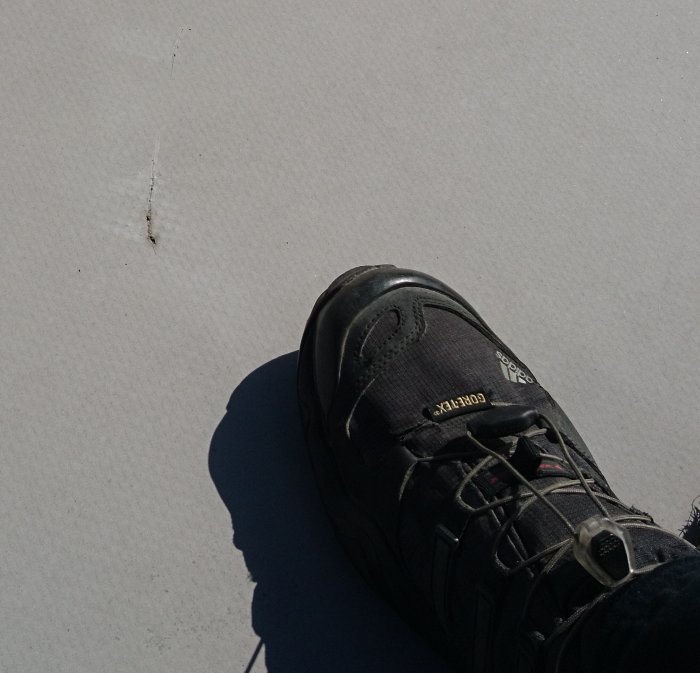 Närbild på vit takduk med mindre repa bredvid en sko för storleksjämförelse.