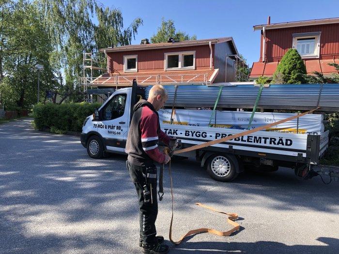 Arbetare bredvid släpvagn lastad med byggmaterial som spontluckor och plåt framför hus.