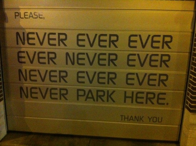 Garagedörr med upprepad text "Please, never ever park here" som humoristisk uppmaning att inte parkera.