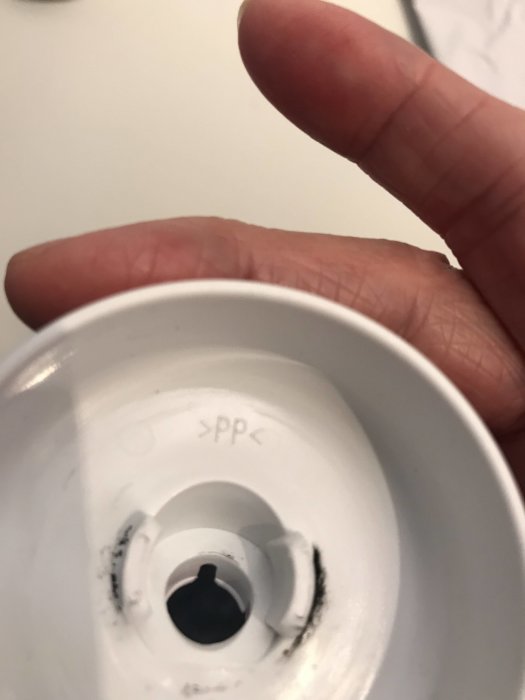 Närbild av en hand som håller en vit ljuskrona med synliga svarta märken och texten ">PPC" inuti.