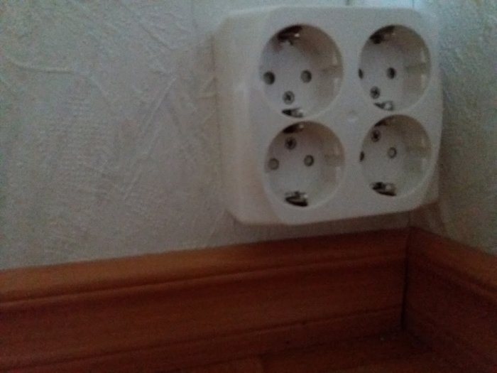 Ett utanpåliggande fyrdubbel-uttag ovanför en golvlist på en strukturerad vägg.