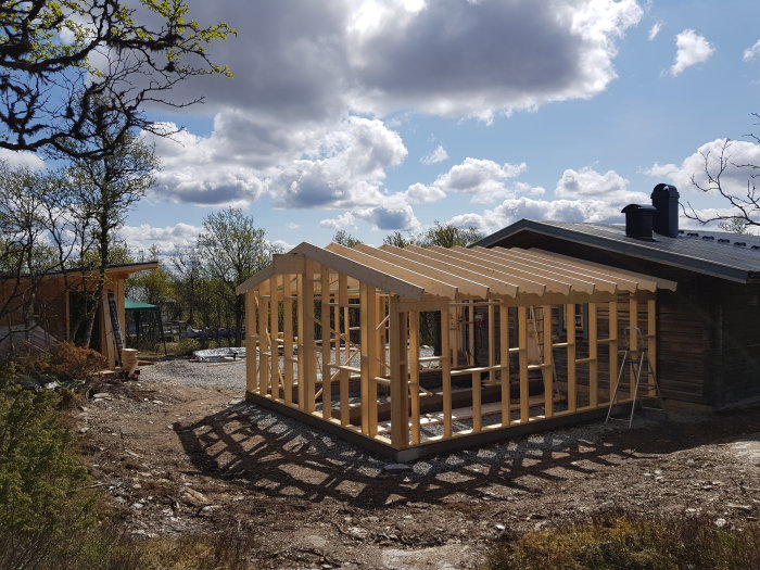 Byggställning för hus med pågående installation av takåsar under soligt väder.