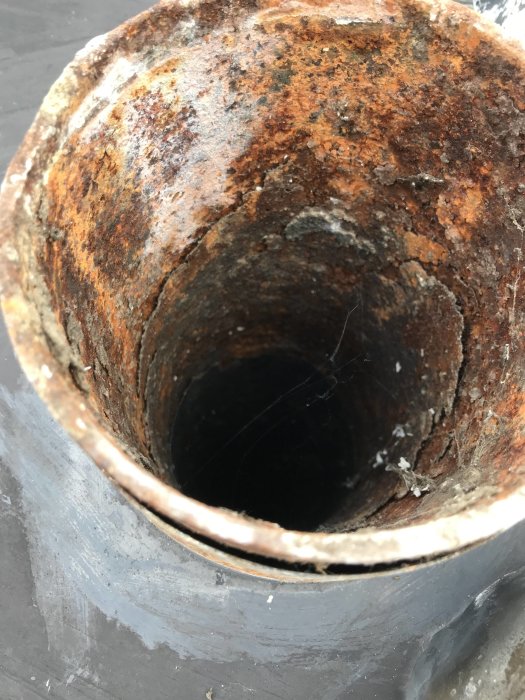 Närbild på det rostiga inre av en tjockare möjlig gjutjärnsrörstopp, möjligen takavvattning.