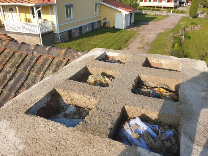 Nyrenoverad skorstenstopp på tak med gammal tegelpannor, redo för skorstenhuv, med hus i bakgrunden.