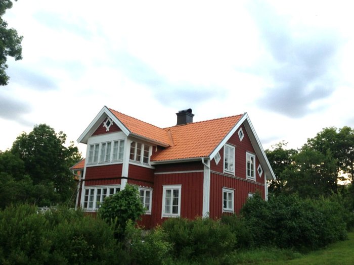 Rött hus med vit snickarglädje och ett högt inbyggt tak som börjar ovanför andra våningen.