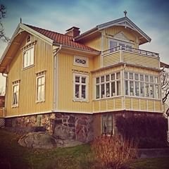 Gult traditionellt hus med veranda och små fönster på andra våningen.