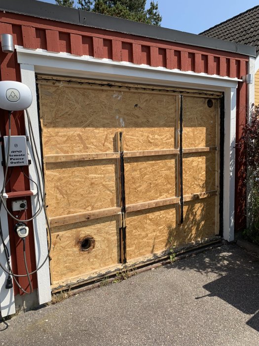 Garage med plywoodvägg där solluftfångare har tagits bort, synliga hål och elkabel.