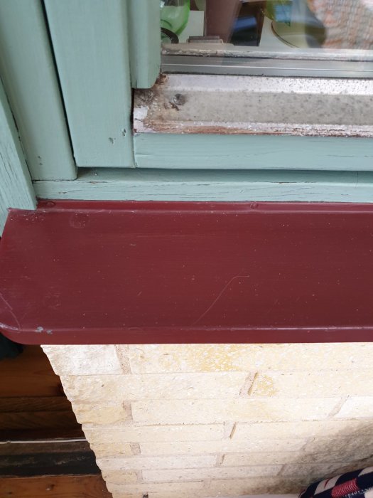 Fönsterbräda med slitage och mögel vid ett äldre fönster mot en tegelvägg.