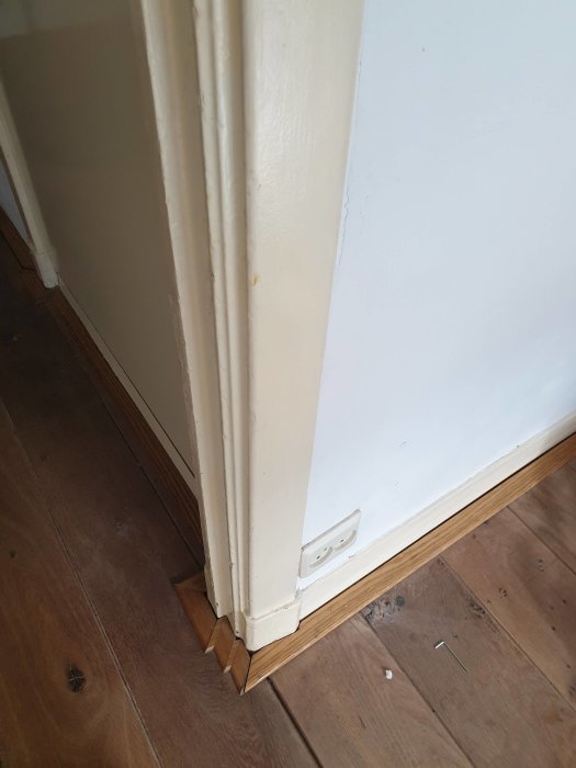Slitna och ojämnt målade dörrlister intill en vit vägg, som behöver renovering.