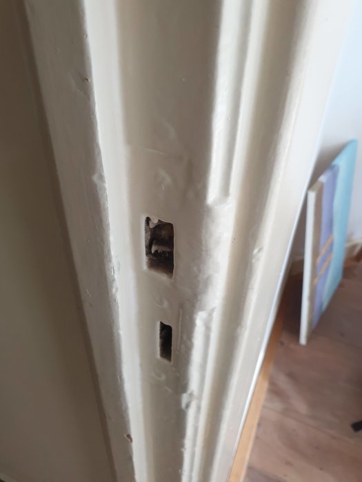 Sliten vitmålad dörrkarm med synliga penseldrag och skador, behöver renovering.