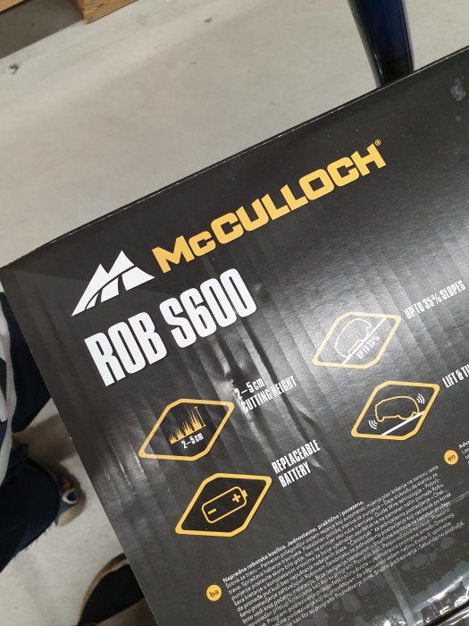 Förpackning av McCulloch ROB S600 robotgräsklippare med information om lutningshantering och utbytbart batteri.