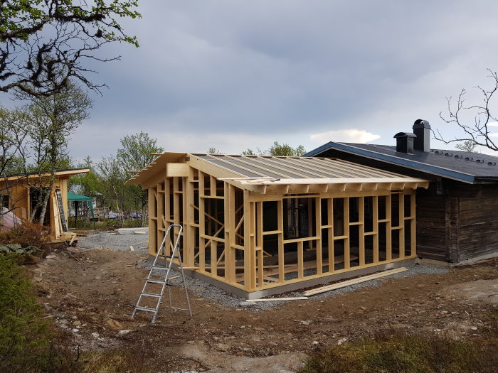 Pågående arbete med råspont på halvklart trähus under mörknande himmel, stege vid sidan.