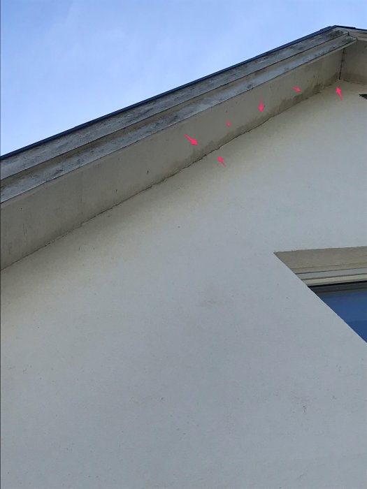 Misstänkt fuktangrepp under takfot på putsfasad av ett hus, markerat med rosa pilar.