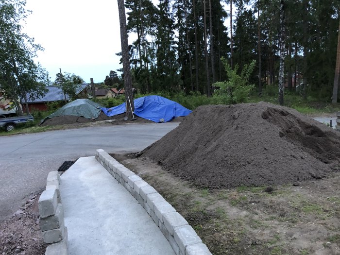 En stor hög kompakt grus bredvid en nybyggd stödmur i en trädgård vid skymningen.