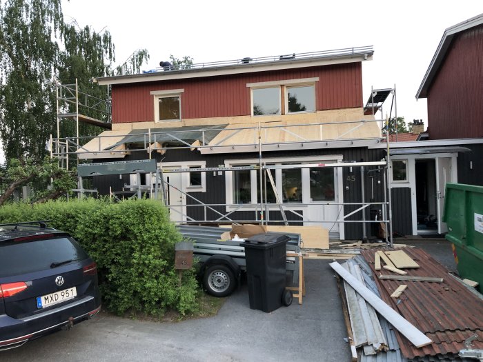 Hus under renovering med nytt tak och ställningar runt fasaden, byggmaterial ligger framför huset.