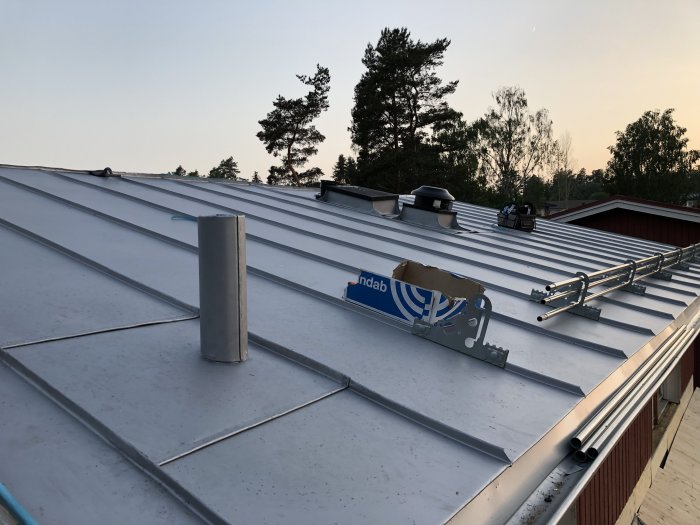 Nyinstallerat dubbelfalsat plåttak med ventilationstrummor och takställning vid skymning.