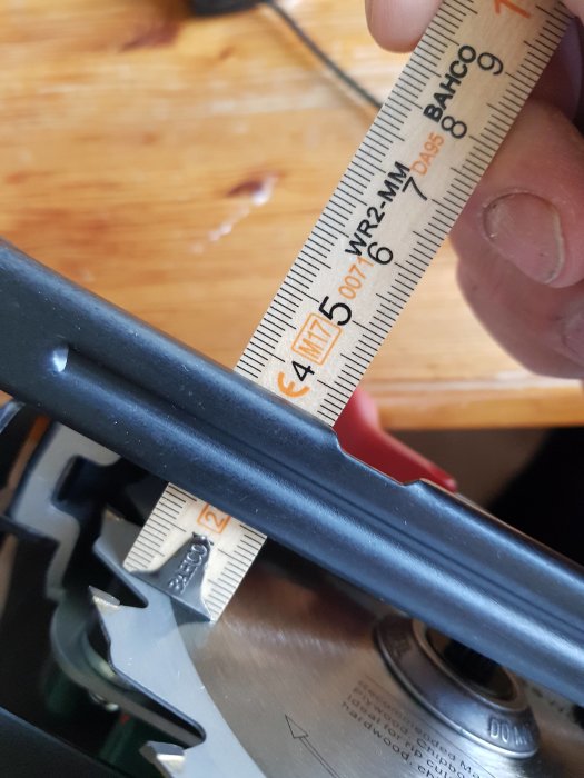 Hand som håller en tumstock mot en maskindel för att mäta och kontrollera linjers räthet under ett byggprojekt.