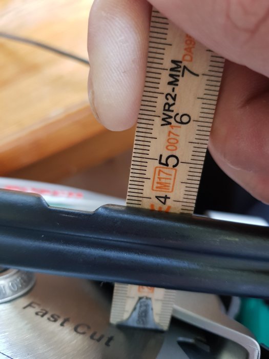 Hand håller en tumstock mot en såg för att mäta vinkeln på klingan i förhållande till sågbordet.