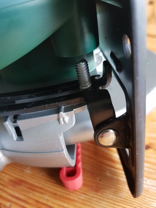 Närbild av en grön maskindel med en borttagen röd plastskruv och en synlig bricka.