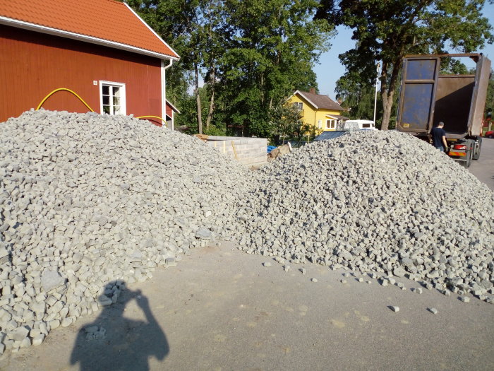 Två stora högar med grus på en byggarbetsplats, leverans från Hasopor-bilen i bakgrunden.