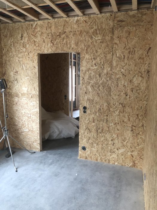 Rum under renovering med OSB-skivor monterade på väggen och en dörröppning.