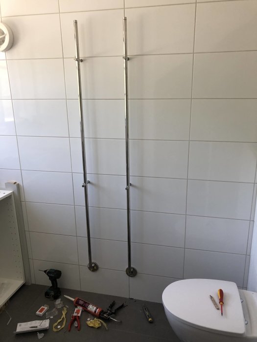 Badrum under renovering med installerad toalett och väntande handdukstorkar, verktyg på golvet.