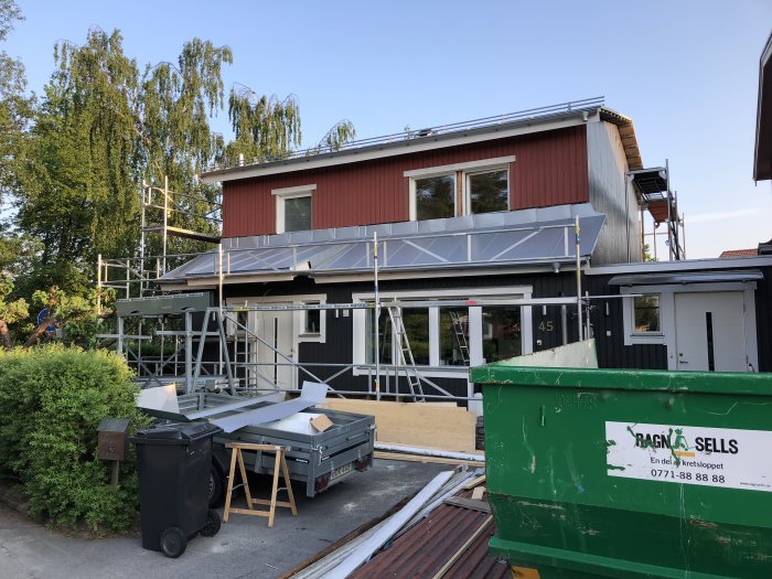 Hus under renovering med nytt tak och ställningar, byggavfall och material synligt i förgrunden.