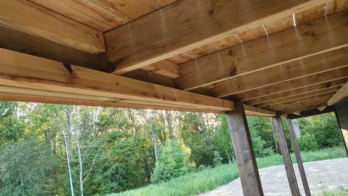 Utsikt under en balkong med träbalkar och stolpar, osäkert infästningssätt syns.