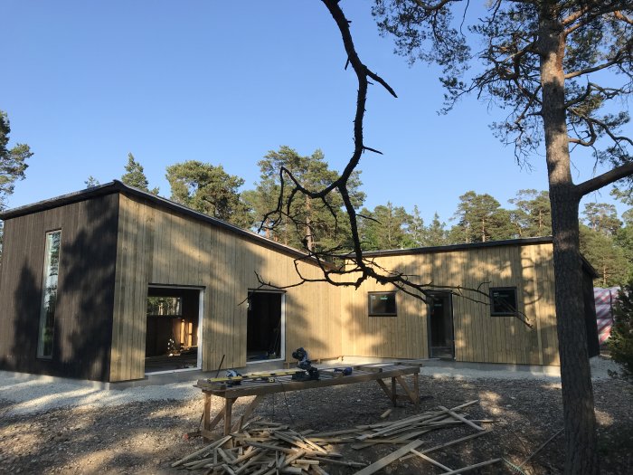 Nästan färdigt hus med panel utomhus omgivet av träd, byggmaterial på marken, utan takplåt och takfot.