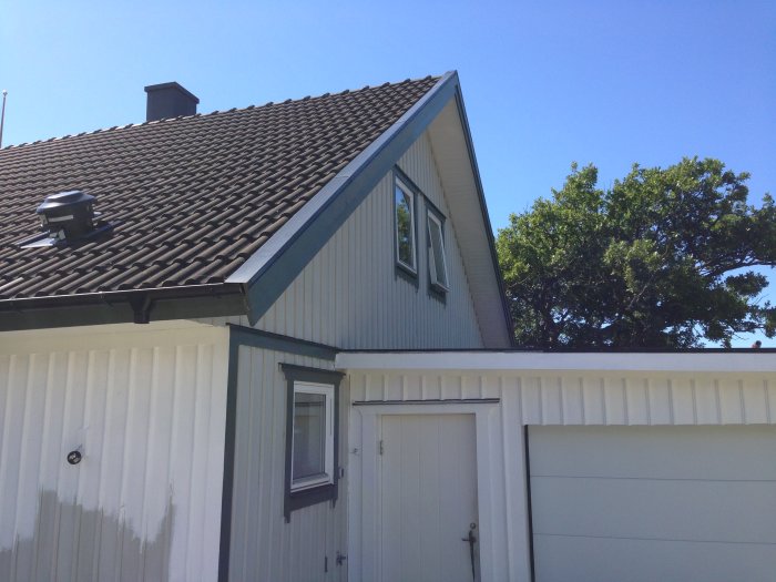 Ett garage med takbeklädnad av ytpapp intill hus med plåttak och utbyggnad.