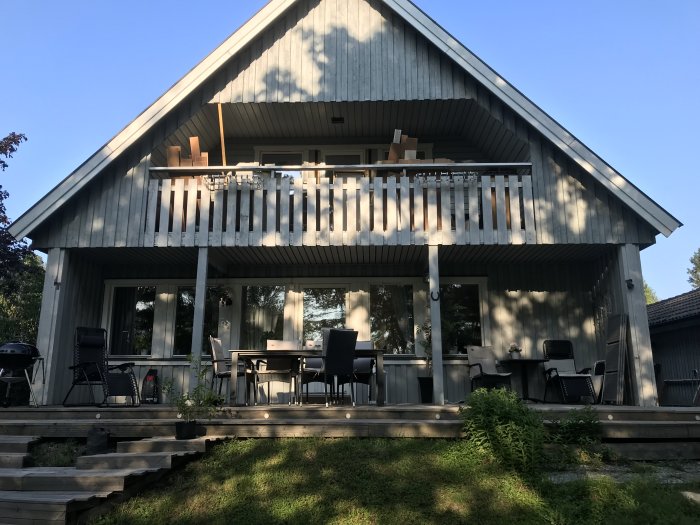Balkong med takstol som stöds av pelare, möblerad med bord och stolar, infälld i ett trähus.