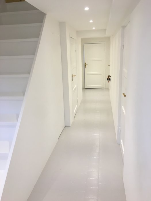 Nyrenoverad korridor med vita väggar, epoxybehandlat golv och stängd dörr i bakgrunden.