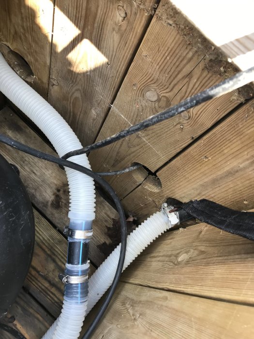 Kabel och vit flexibel slang som leder in under träplattform, tecken på vattenpåverkan synligt.
