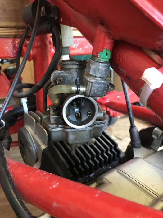 En förgasare monterad på en motor inuti en ram med röd färg.