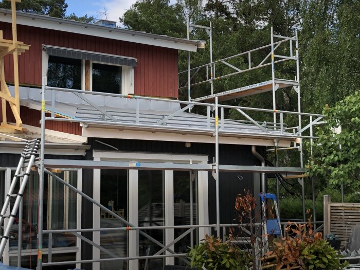 Hus under renovering med tillfällig taklucka, ställningar och snörasskydd på taket.