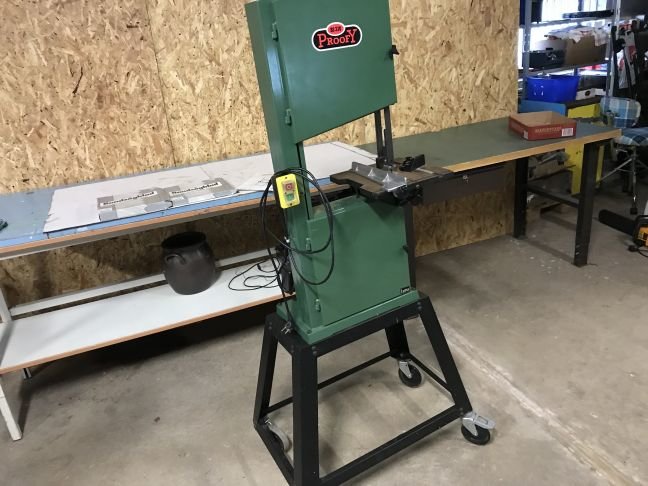 En bandsåg i ett verkstadsutrymme med bord och arbetsmaterial i bakgrunden.