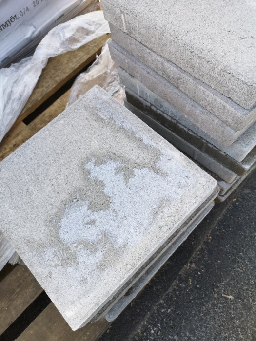 Betongplatta med kalkutfällningar ovanpå en pall med andra gråa plattor.