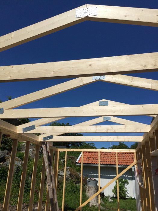 Nyinstallerade trä-takstolar på en byggarbetsplats mot en klarblå himmel.