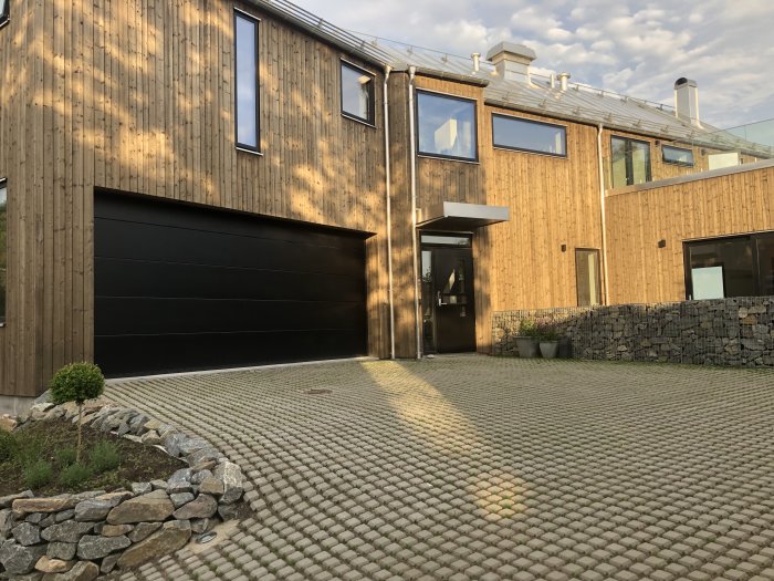 Modern villa med gräsarmering i betong framför garage, blockmönstrad yta med gräs mellan stenarna.