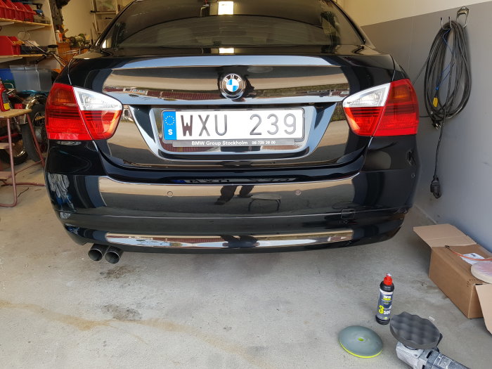 Välputsad svart BMW bakifrån i ett garage med putsmedel och polerutrustning på golvet.