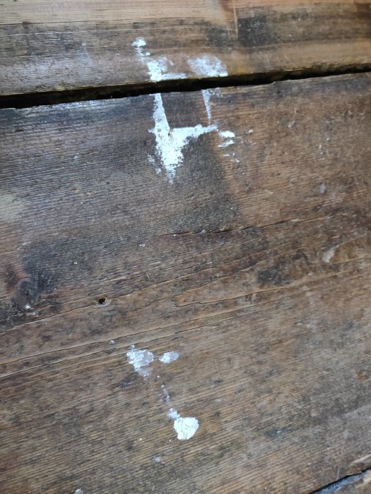 Slitet trägolv med stora springor och målarfärgsfläckar på ytan som behöver renovering.