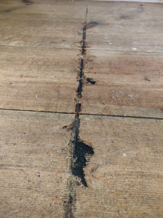 Närbild av slitet trägolv med stor springa och skador.
