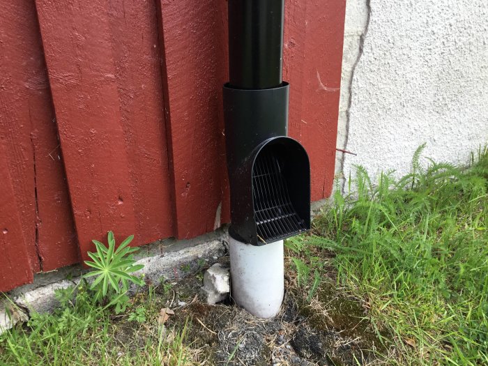 Svart nedrör med möss/borrhålsskydd mot en röd vägg och vit sockel, eventuellt blekt från orange.