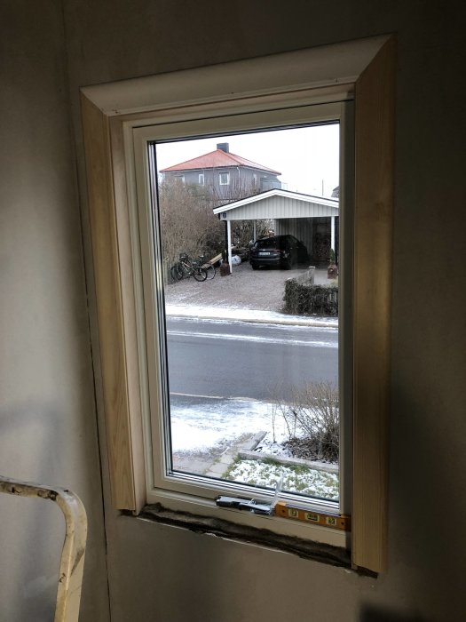 Nyinstallerat fönster med utsikt mot snötäckt uppfart och hus med carport.